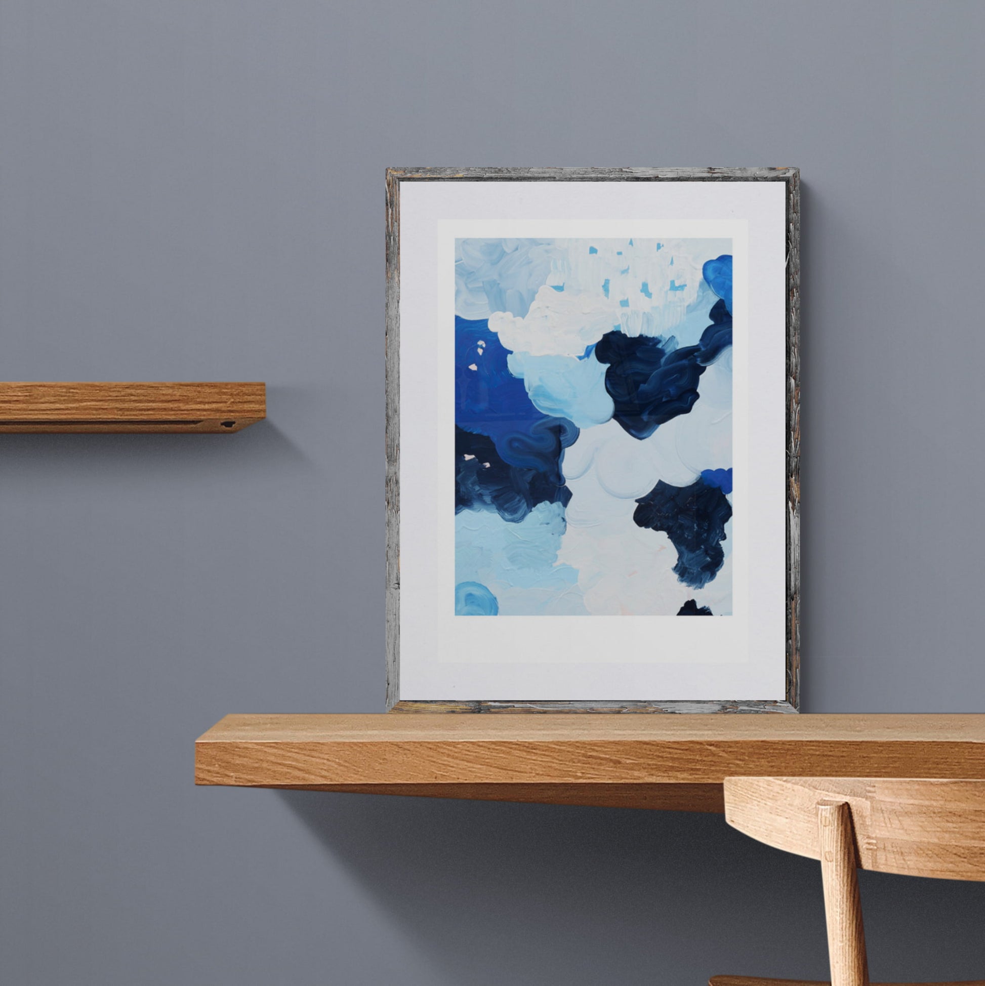Abstract print of blues, white and grey clouds depicting Antarctica framed and leaning on a shelf.