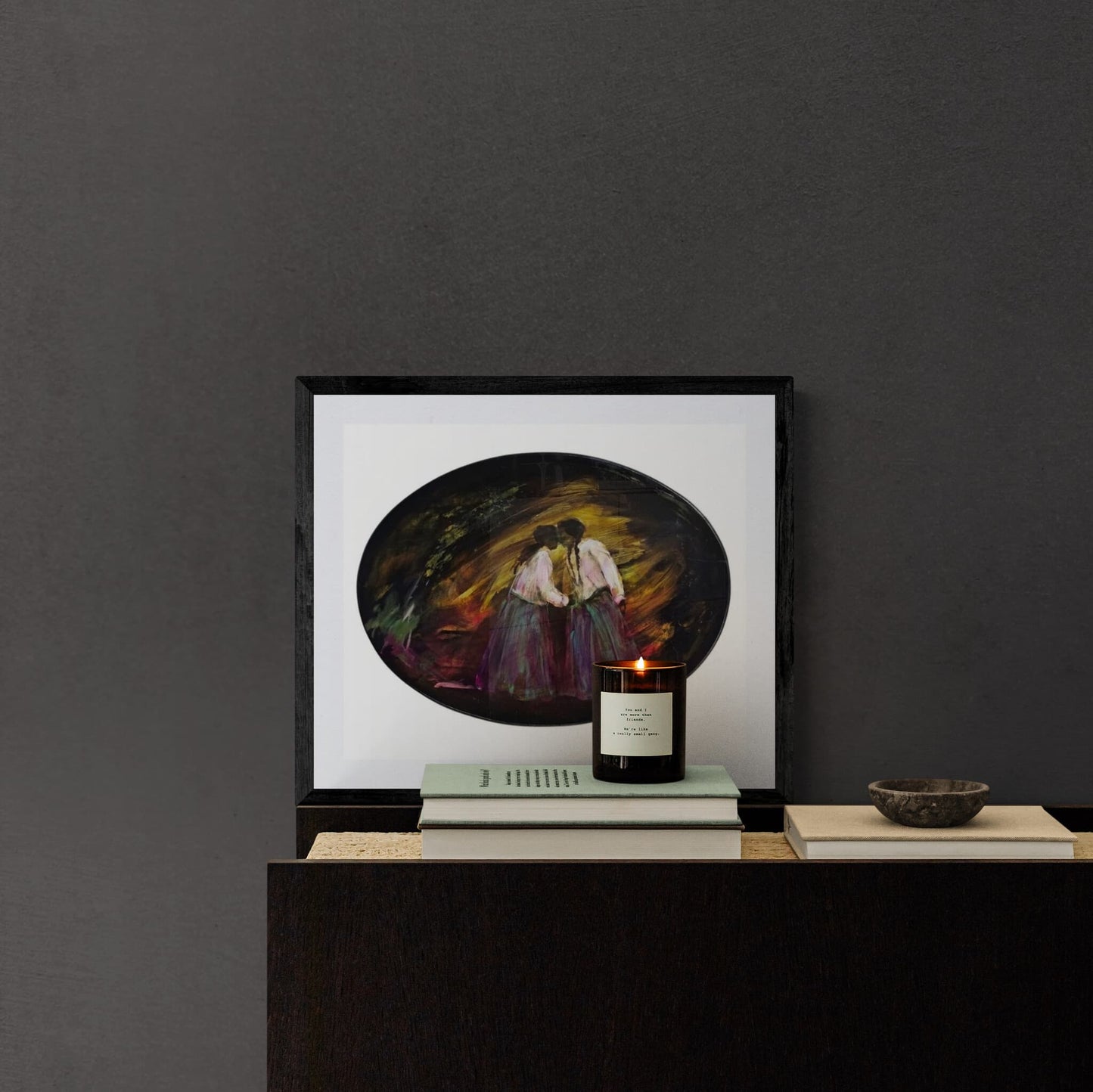 Framed artwork of two sisters on a dark surface with a candle and small bowl.