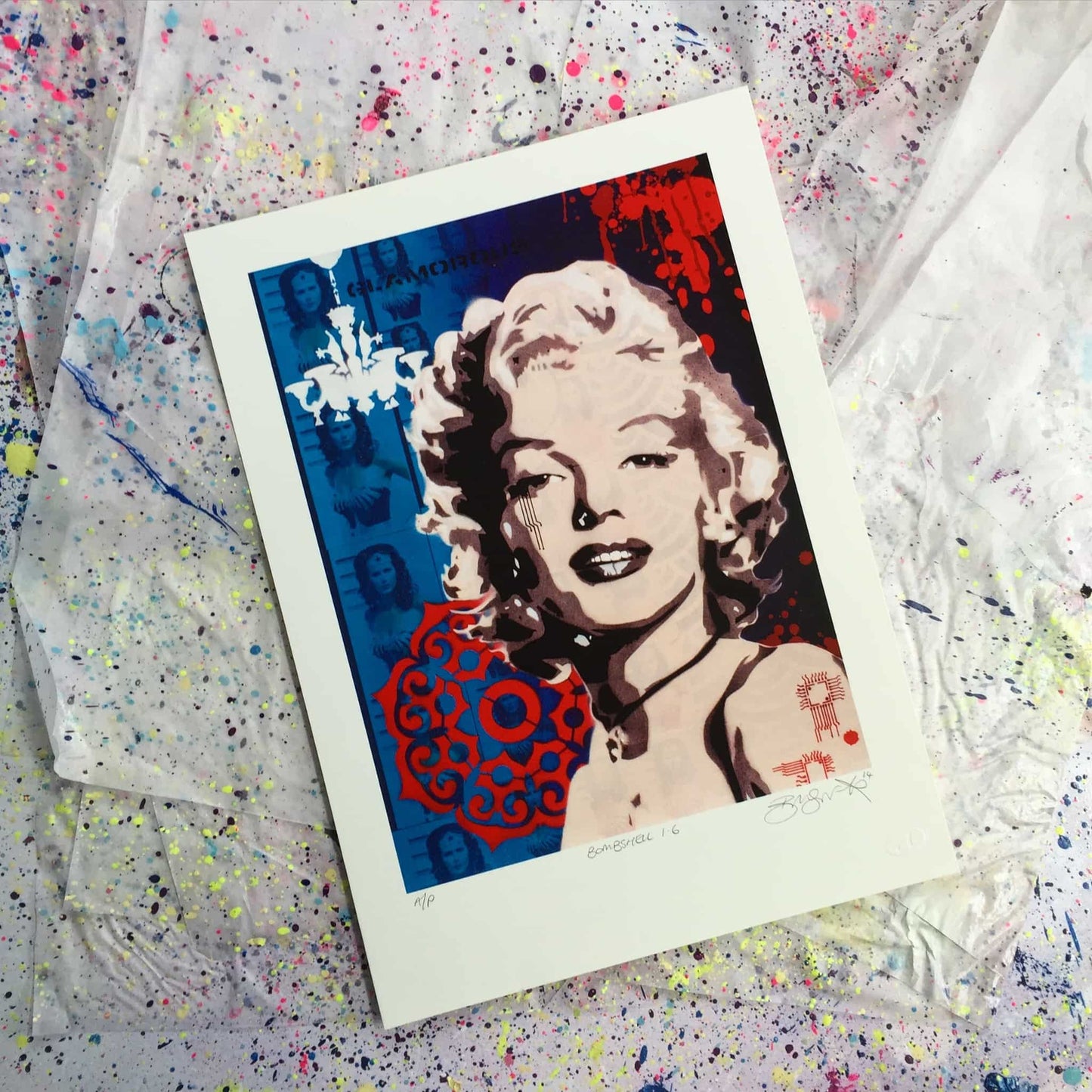 Stunning screenprint of Marilyn Monroe on blue and red background. Images of Wonder Woman are repeated in the background. Print is lying on paint splattered paper.
