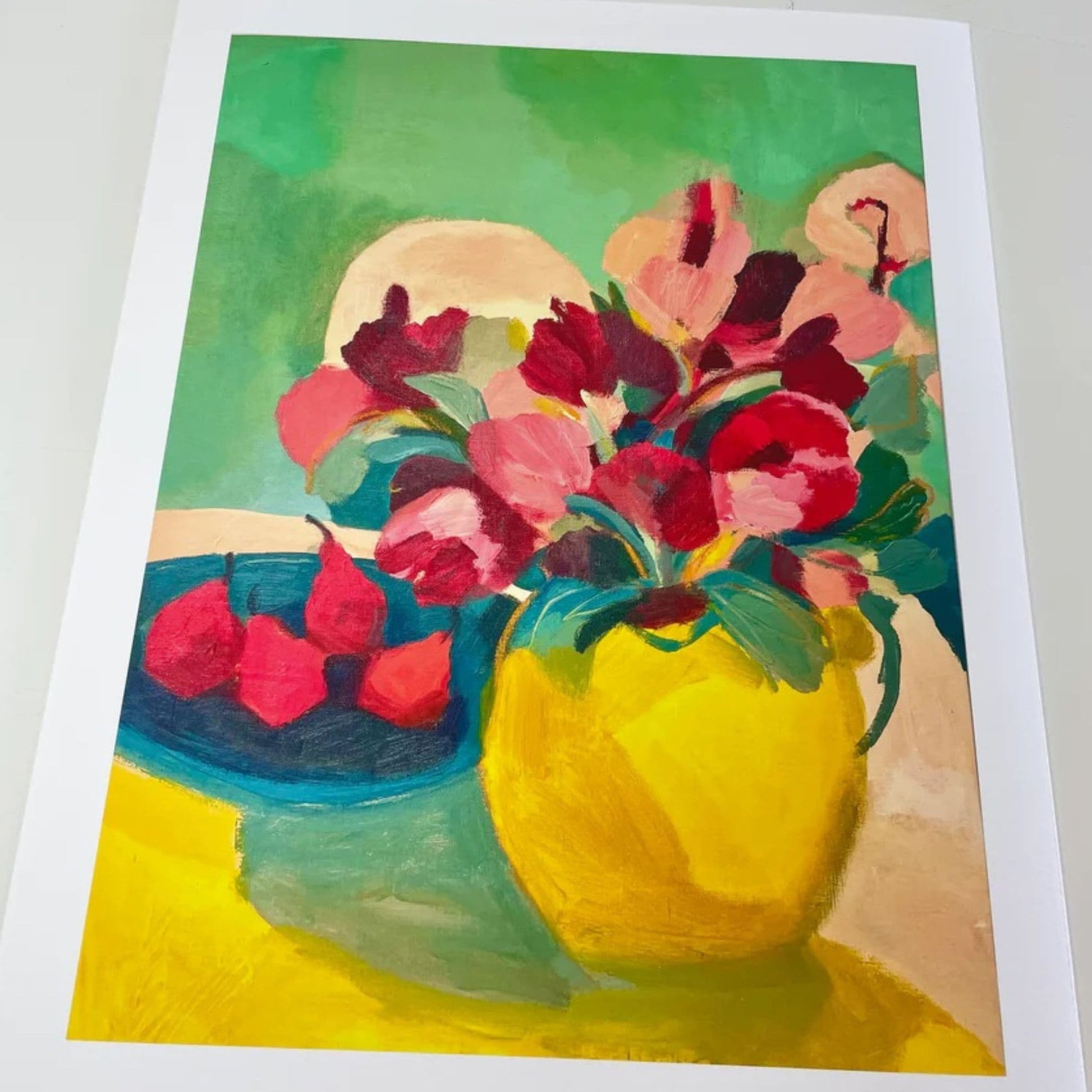 Yellow vase with red flowers and blue bowl with red pears in it.