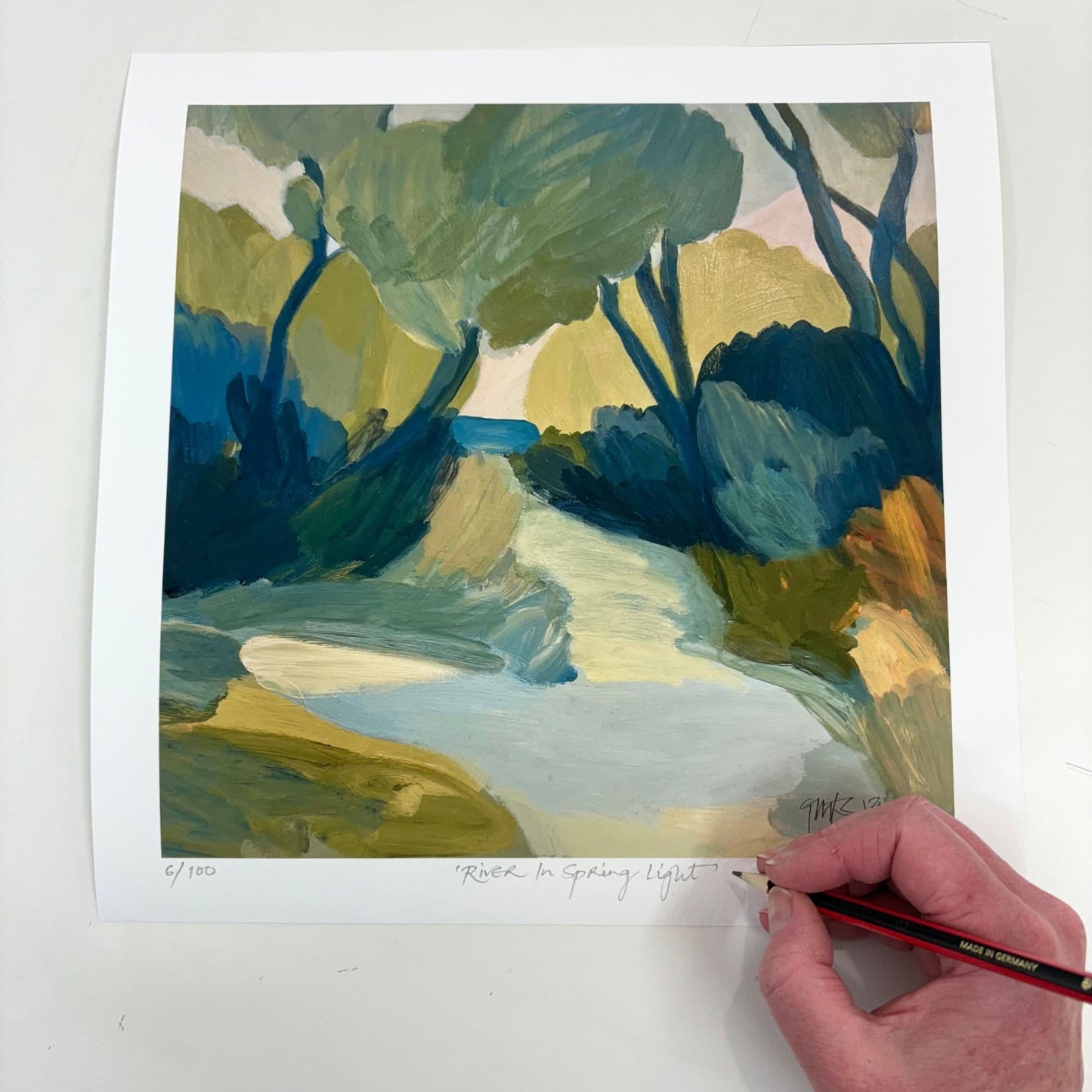 Hand signing Georgina Hoby Scutt's "River in Spring Light" limited edition print – A vibrant river scene where light and shadow dance across rich blues.