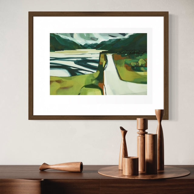 Scenic view of a river crossing surrounded by rugged mountains and lush alpine landscape, framed and hanging above a sideboard