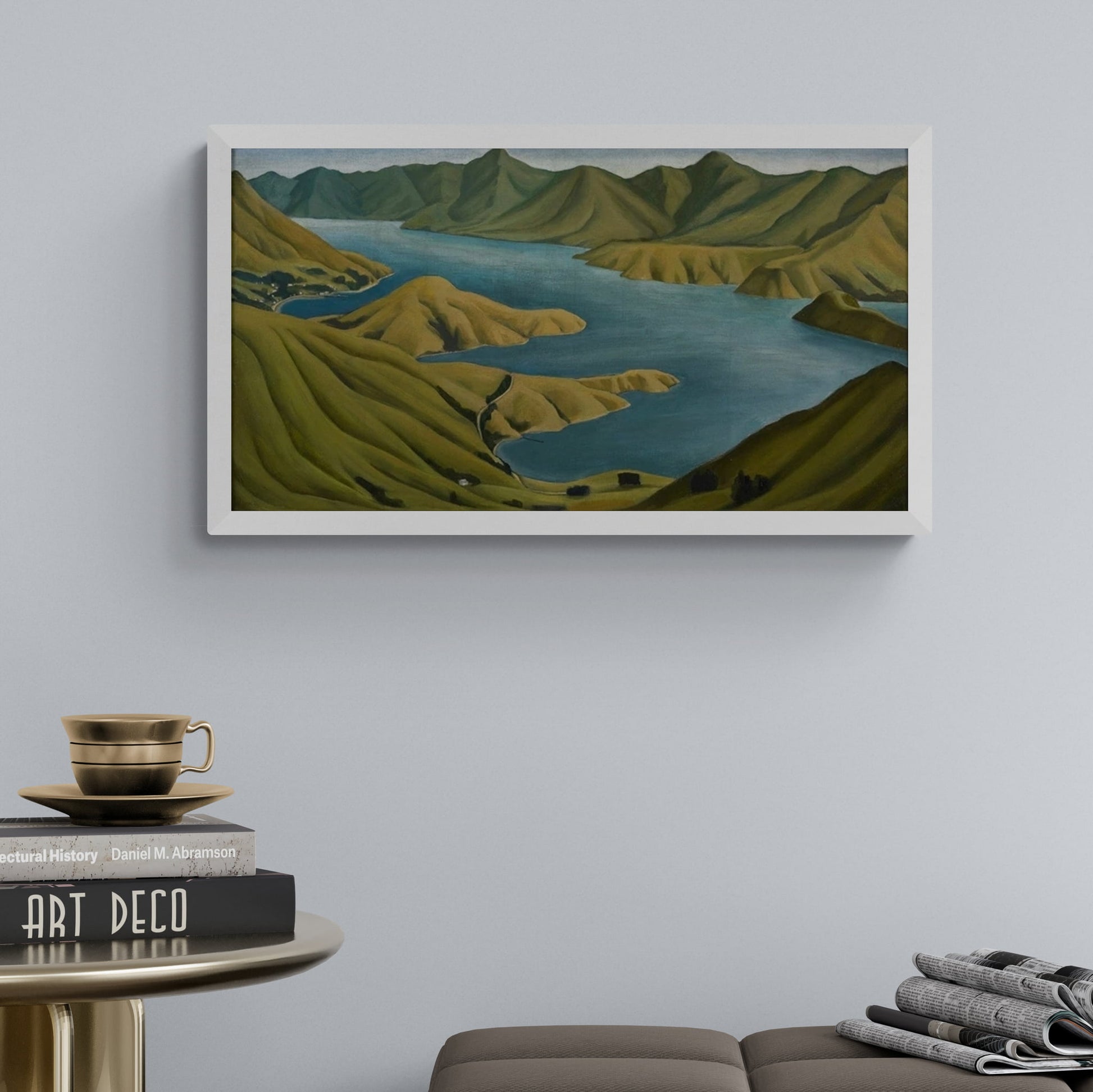 Print of the Akaroa harbour landscape with rolling green hills and blue water framed and hanging on wall.