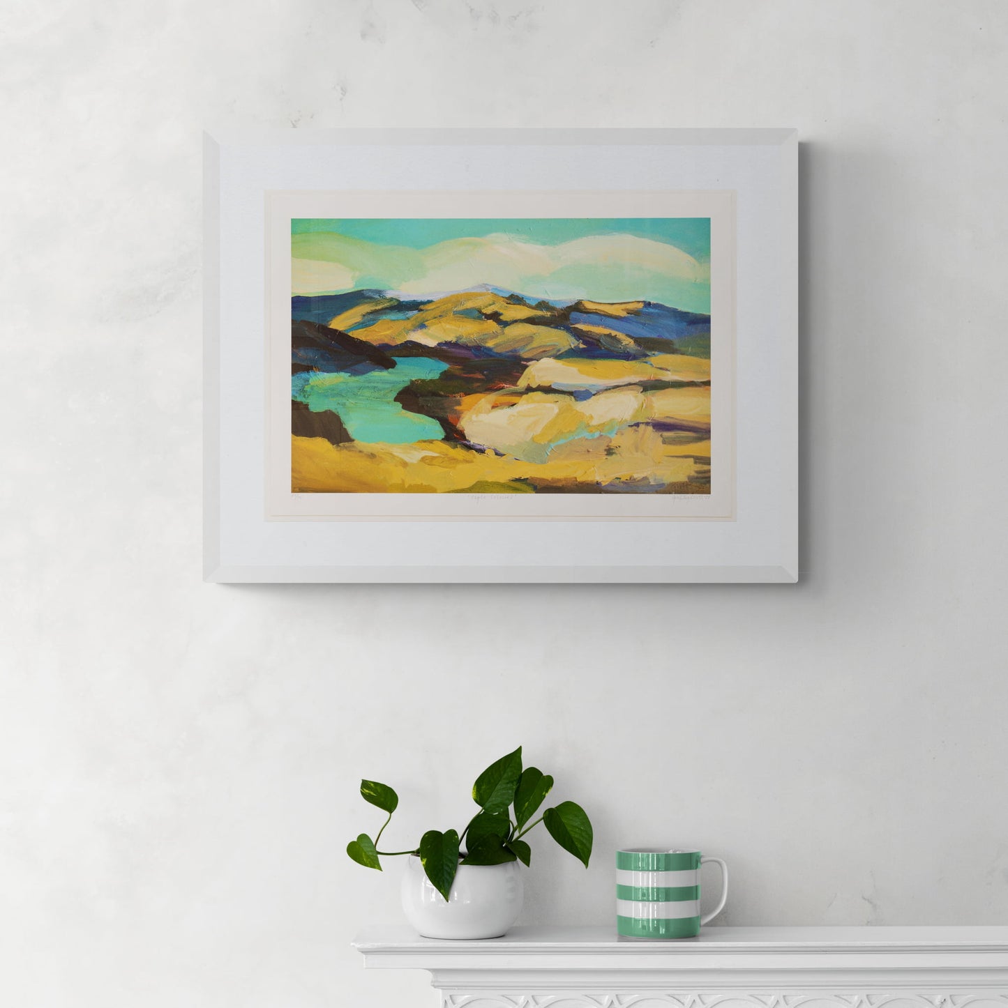 Framed landscape print of yellow hills and the vivid blue Clutha river around Clyde hanging on white wall.