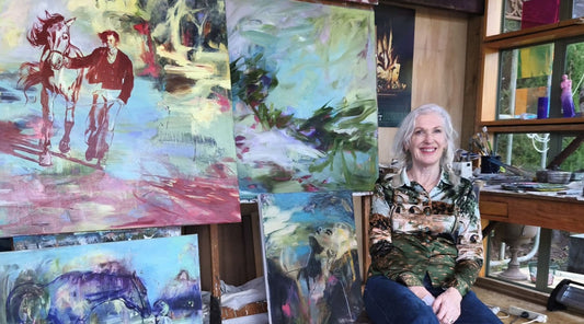 Portrait of artist Anita DeSoto seated in her studio, surrounded by her large-scale figurative oil paintings.