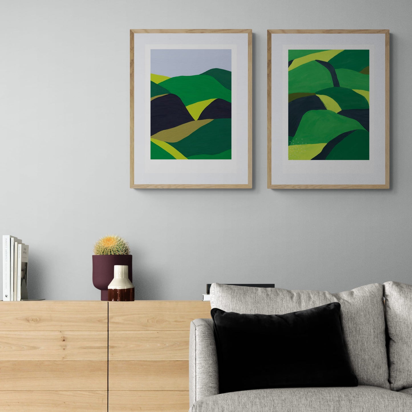 Two framed landscapes of greens and black rolling hills hanging above couch and dresser. om wall.