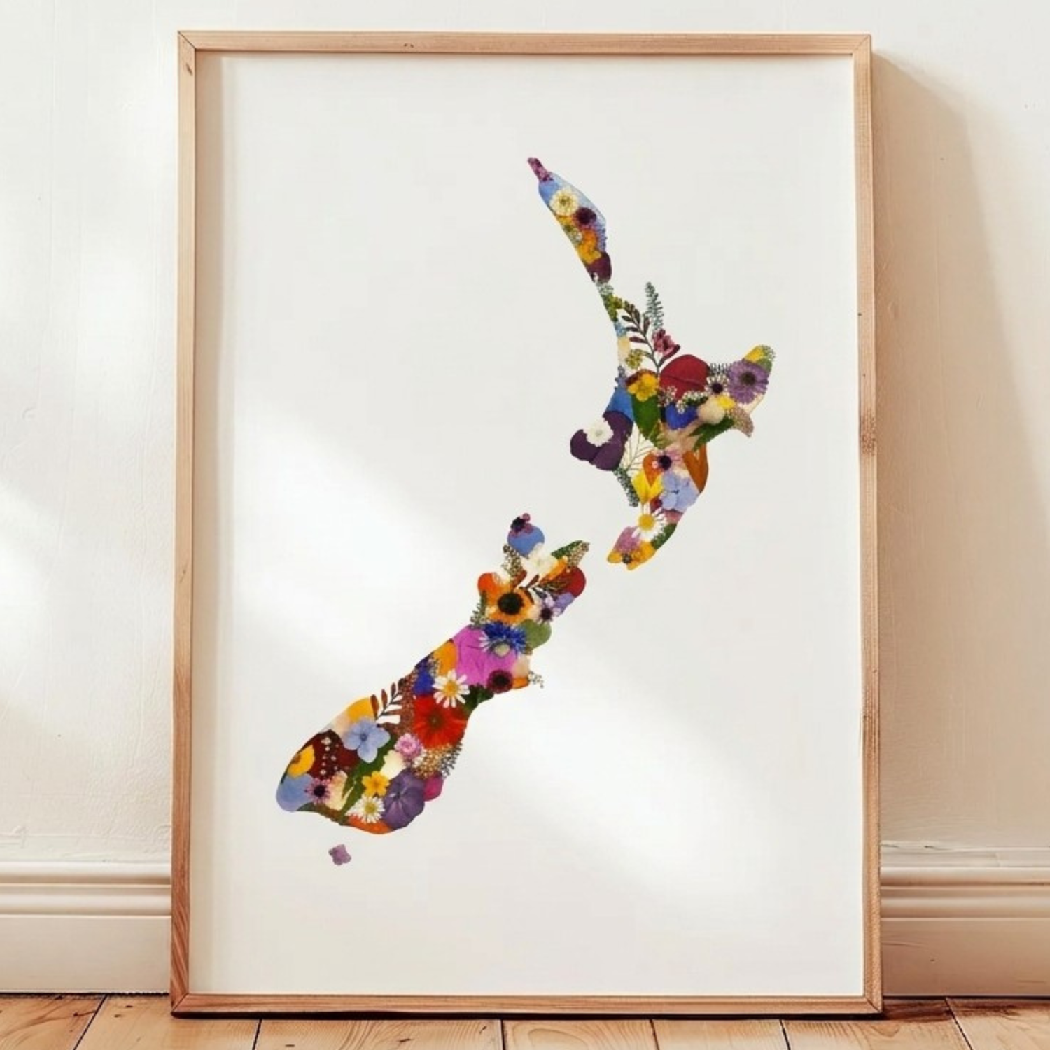 Framed artwork of a colorful pressed floral map of New Zealand on a white wall.