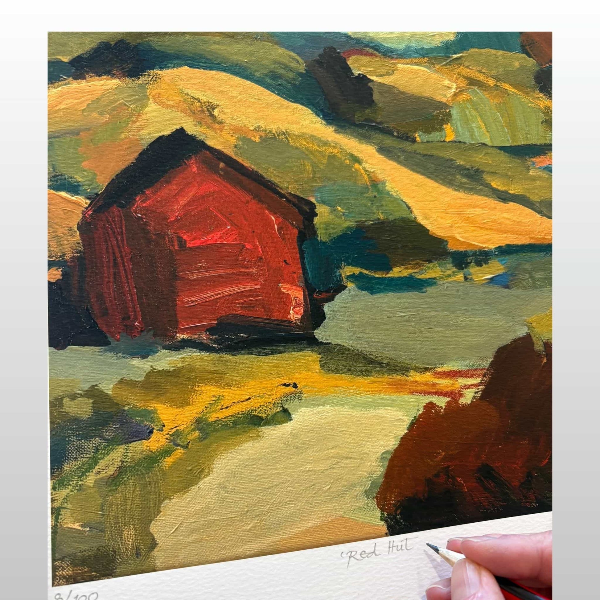 Print of a red barn in a landscape with a hand  holding a pencil to name and sign it