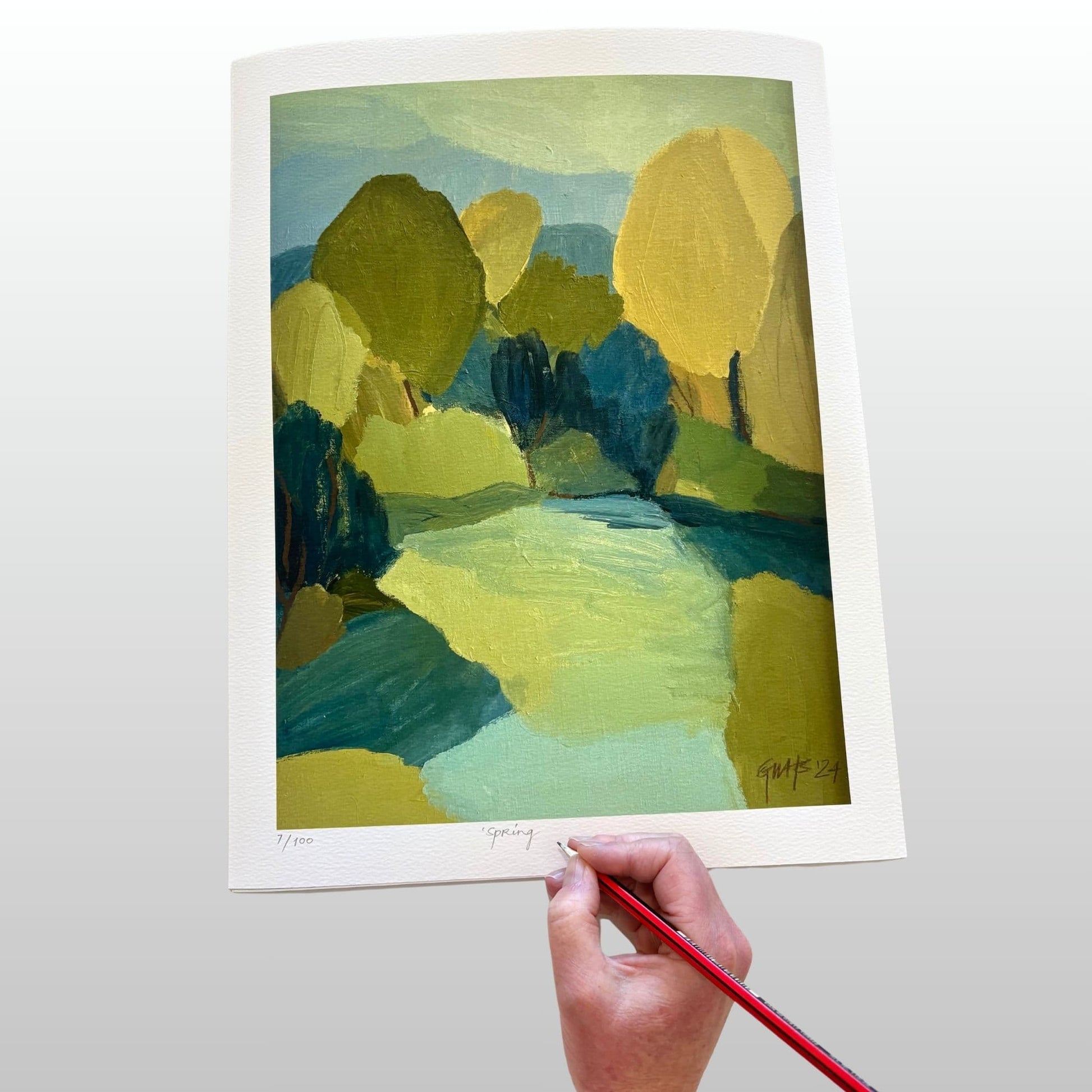 Artist signing an abstract landscape artwork with green, yellow and blue colours.