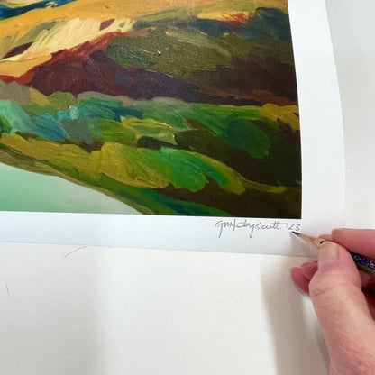 Artist signing a print of the Crown Range with the bright blue Cardrona River in the foreground.