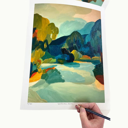 Artist signing a print of river landscape scene in vibrant blue and green colours