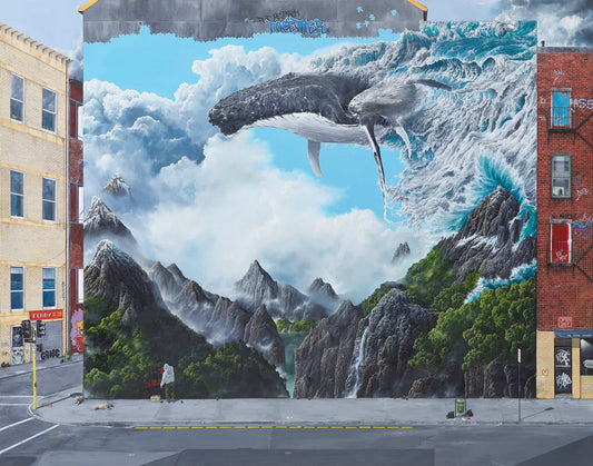 Mural of a whale emerging from water with mountains and a person in the foreground on a city street.