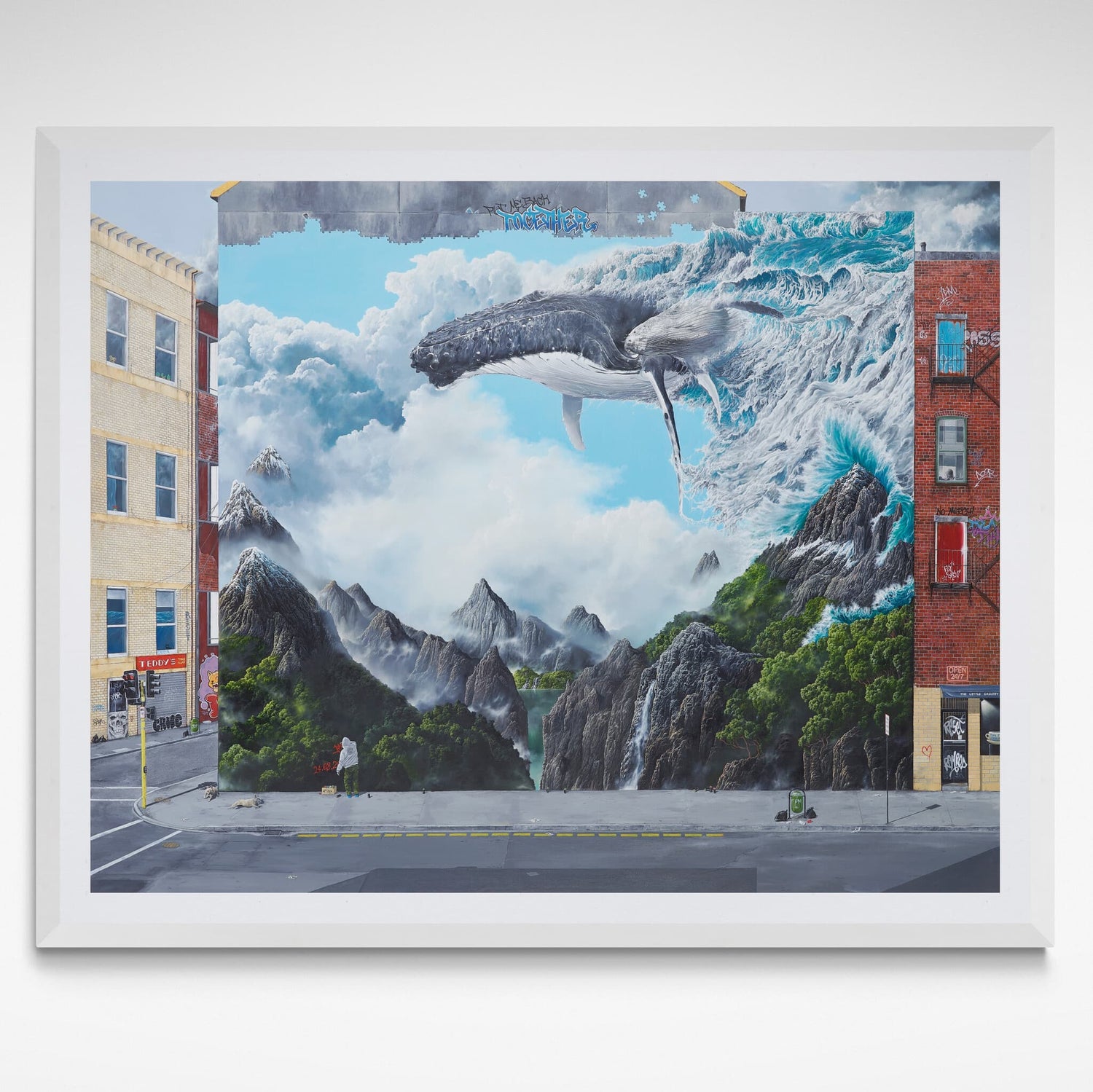 Framed artwork of a whale emerging from a mountain landscape with buildings.
