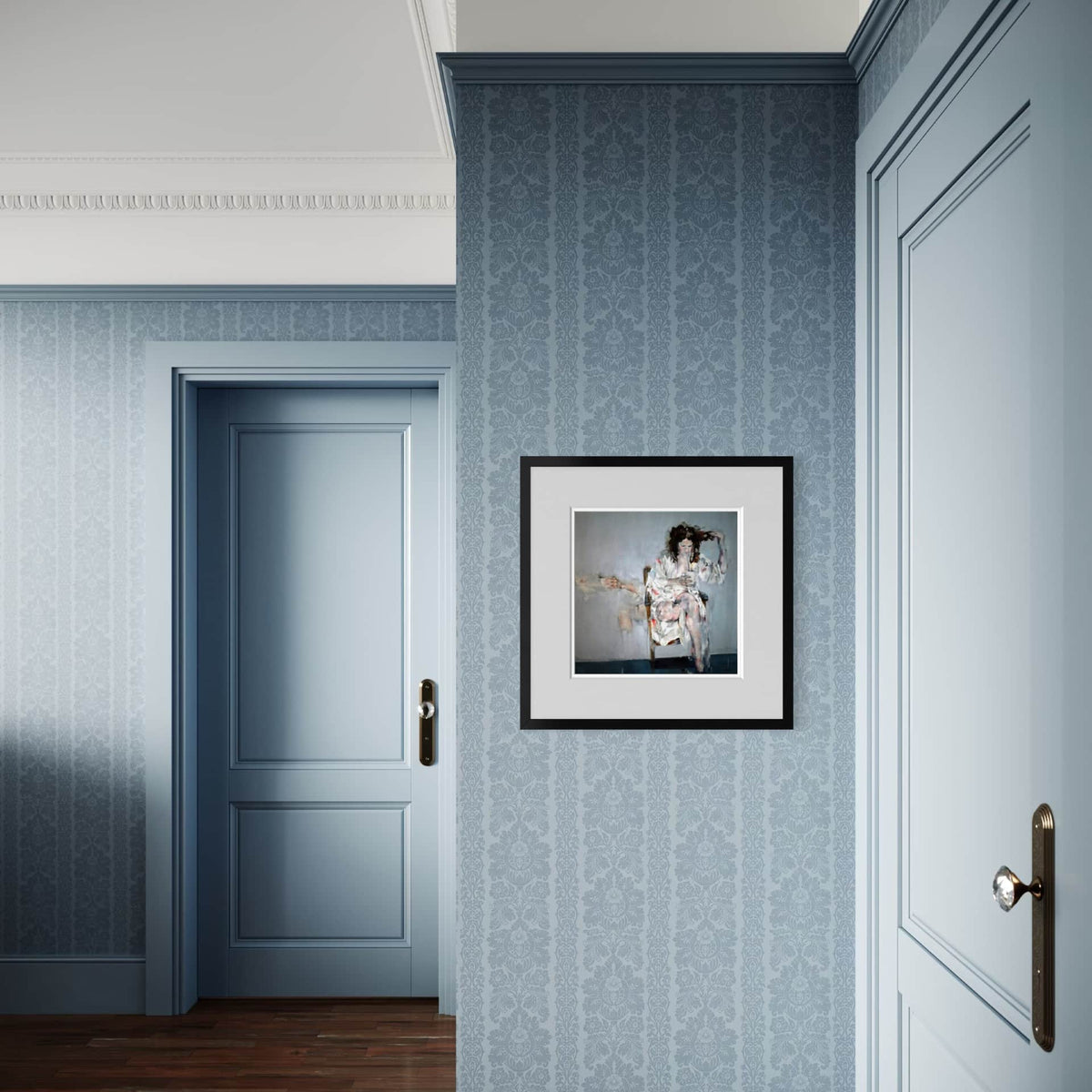 A framed art print featuring an abstract painting of a woman, displayed on a blue patterned wallpaper wall in a hallway with blue doors.
