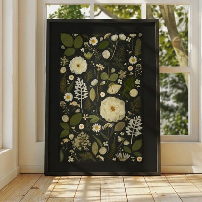 Framed botanical artwork with white flowers and green leaves on a black background, displayed in a room with natural light.