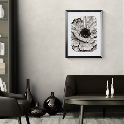 A framed Solstice Studio black and white flower print featuring a large detailed flower with expressive black lines on a cream background hanging above a brown couch.