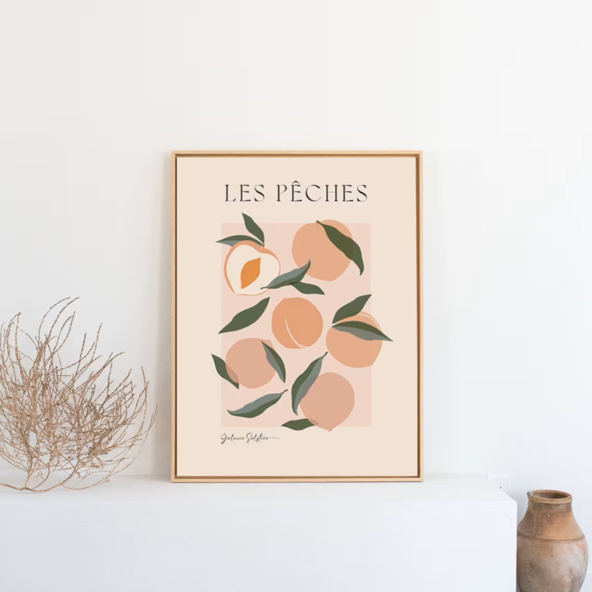 Framed print of peaches with green leaves sitting ona shelf.