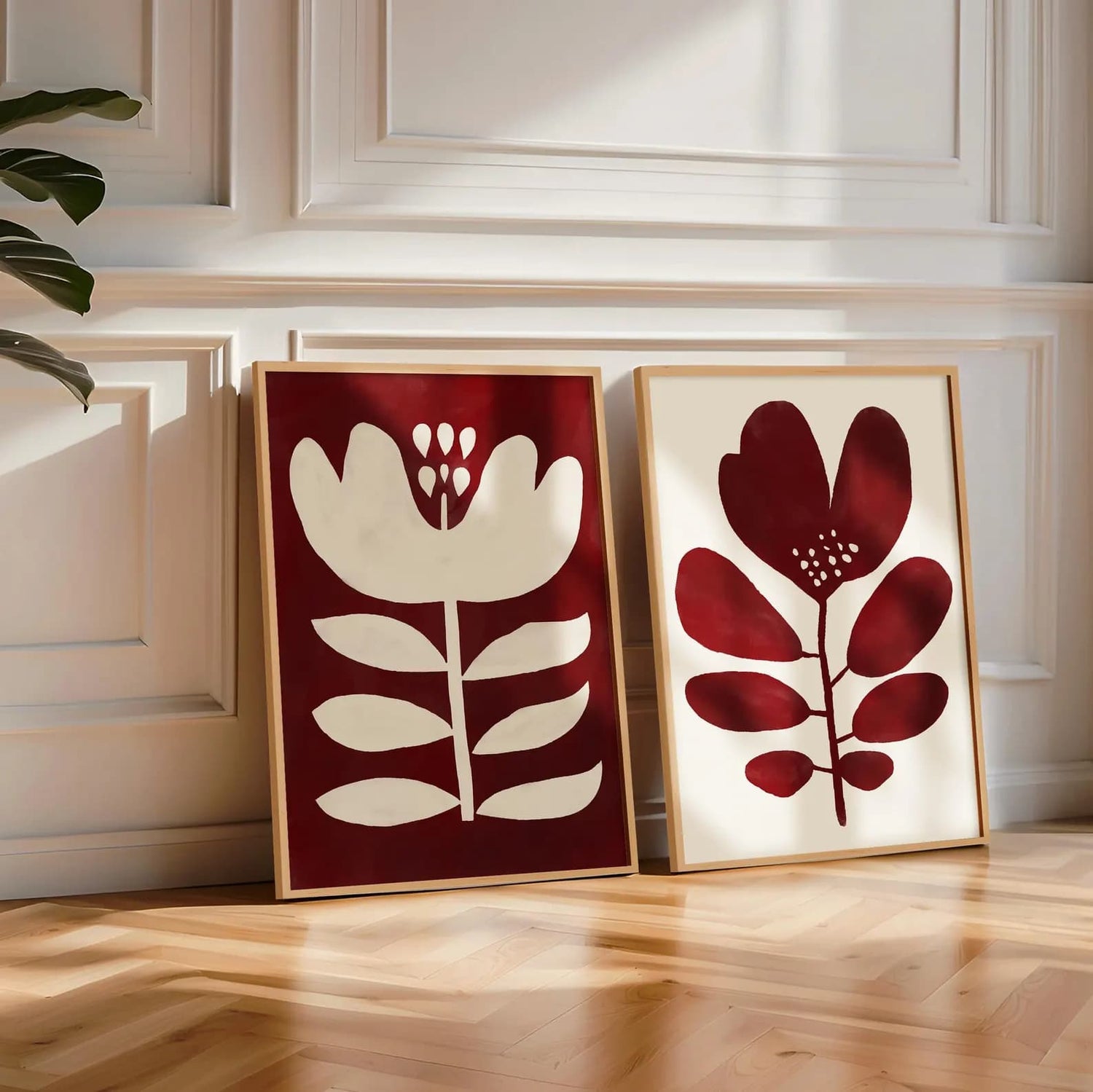 Two framed dark red floral and leaf prints by Solstice Studio on a wooden floor with a white wall background