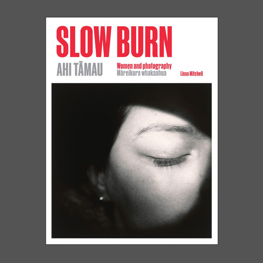 Book cover for 'Slow Burn Ahi Tämau', by Lissa Mitchell, featuring a black and white close-up photograph of a person's face with one eye closed, on a white background with red and grey text.