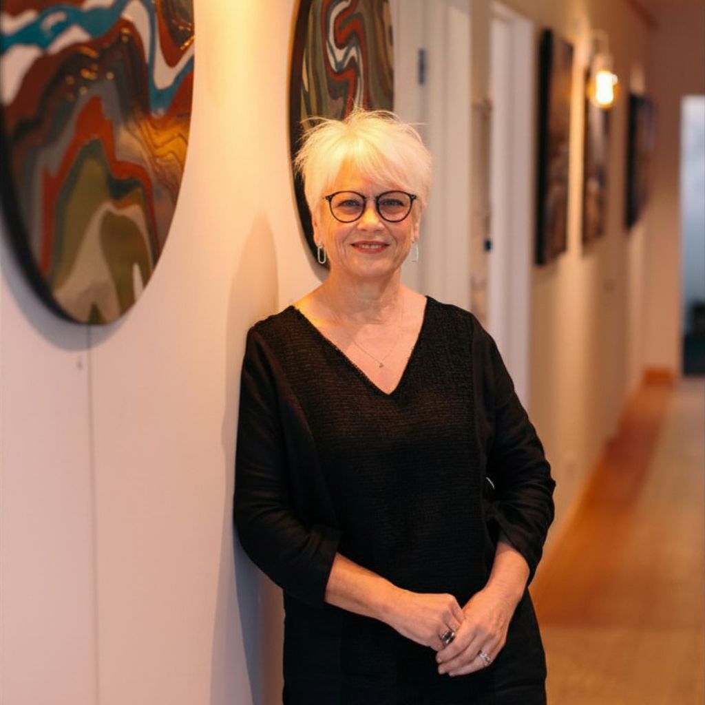 Owner, Jan McPhedran, standing in a gallery of paintings by Diana Adams