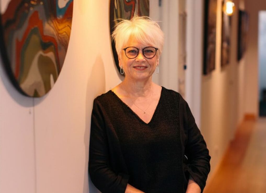 Look NZ owner Jan McPhedran standing in an art gallery with paintings on the wall.