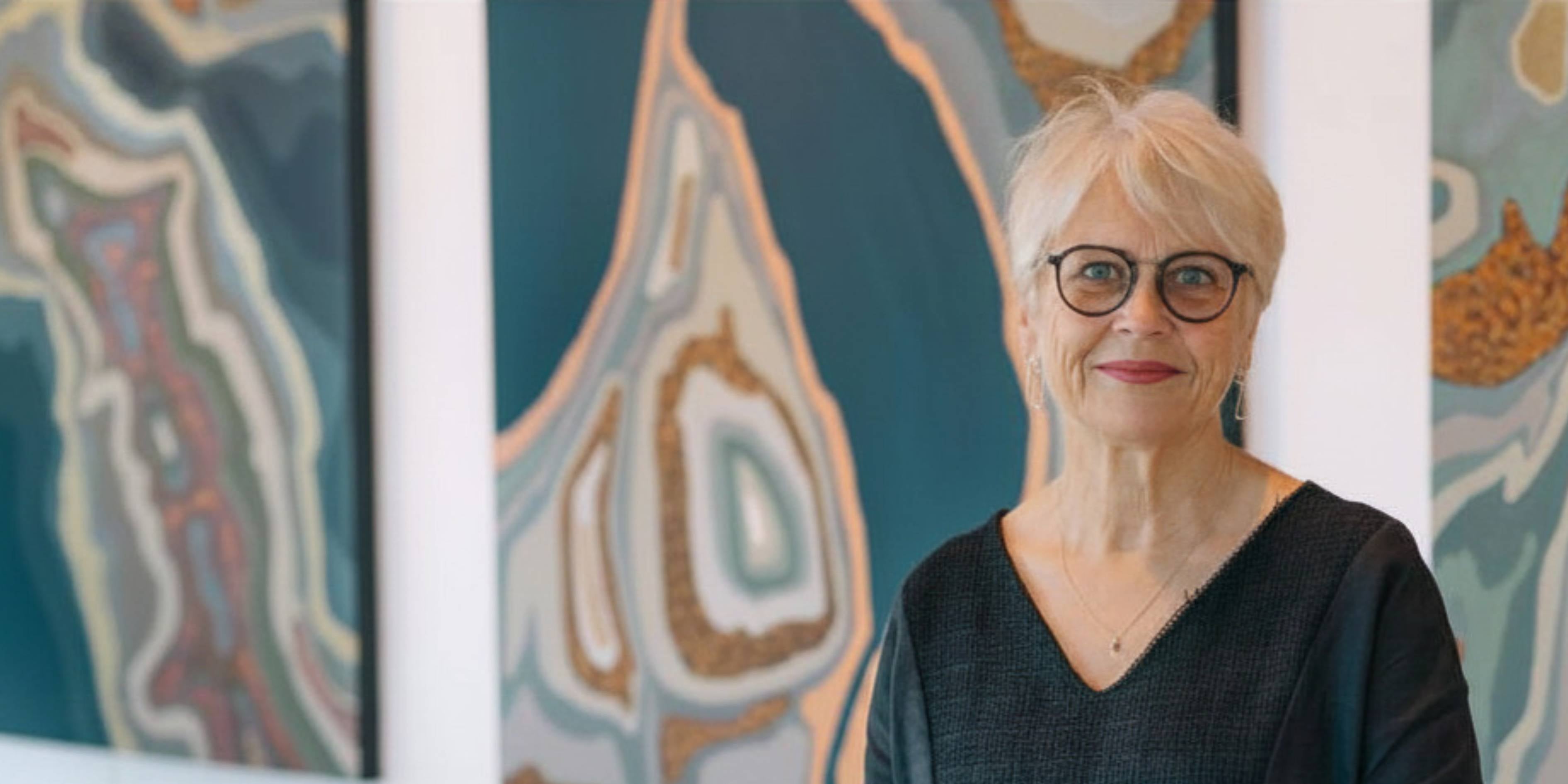 Owner Jan, standing in front of large paintings by Diana Adams
