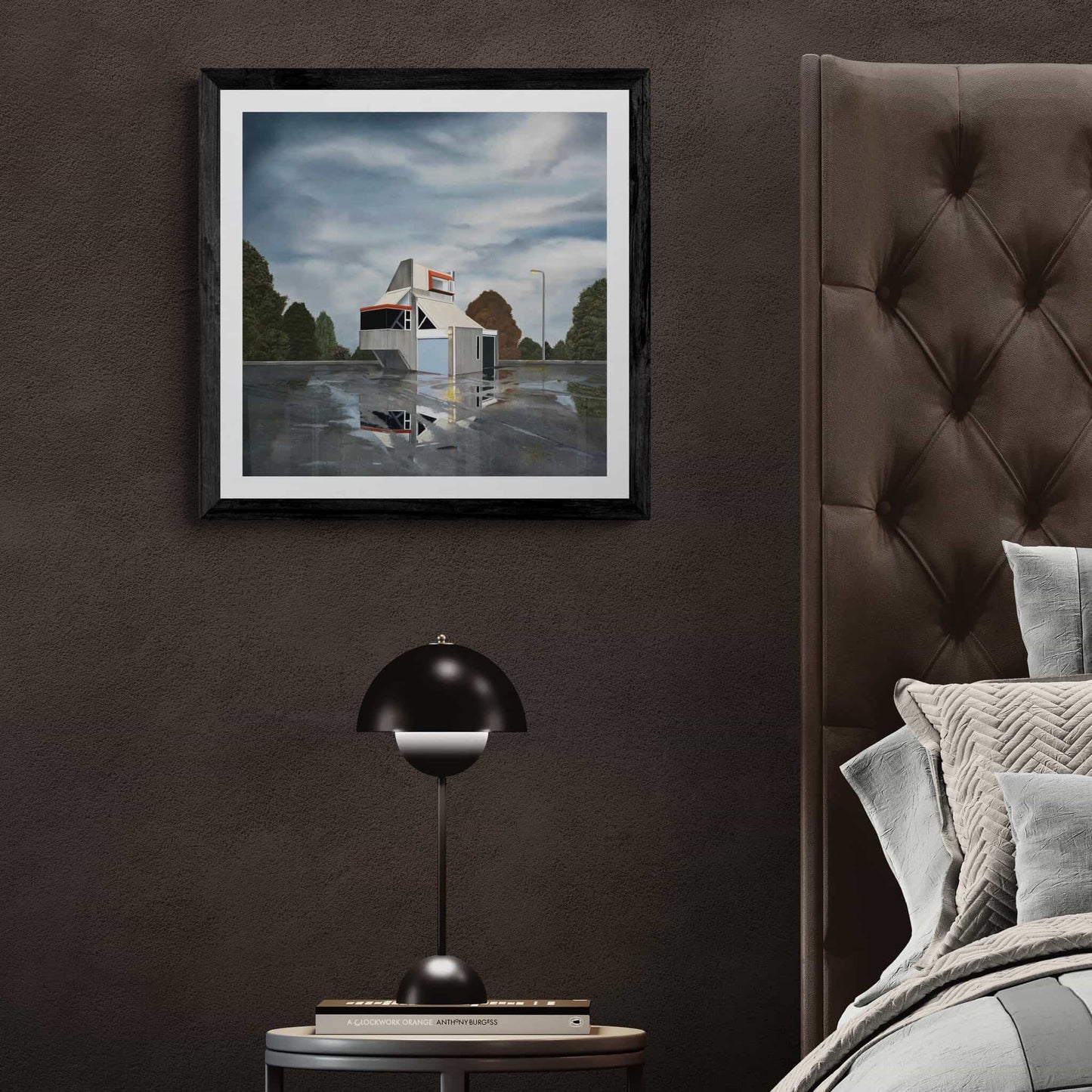 Framed artwork of an abandoned building with reflection on a wall above a bed with a dark headboard