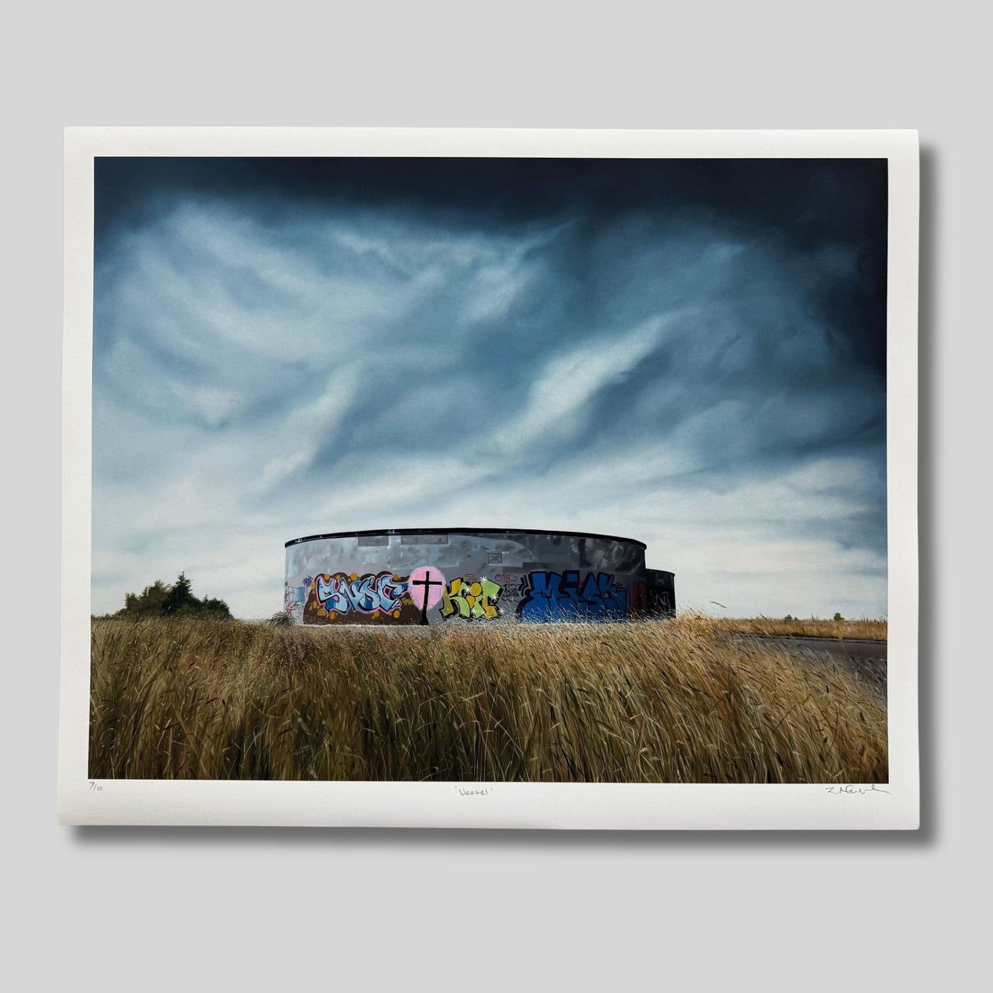 Artwork of a round concrete structure with graffiti on a grassy field under a dramatic sky.