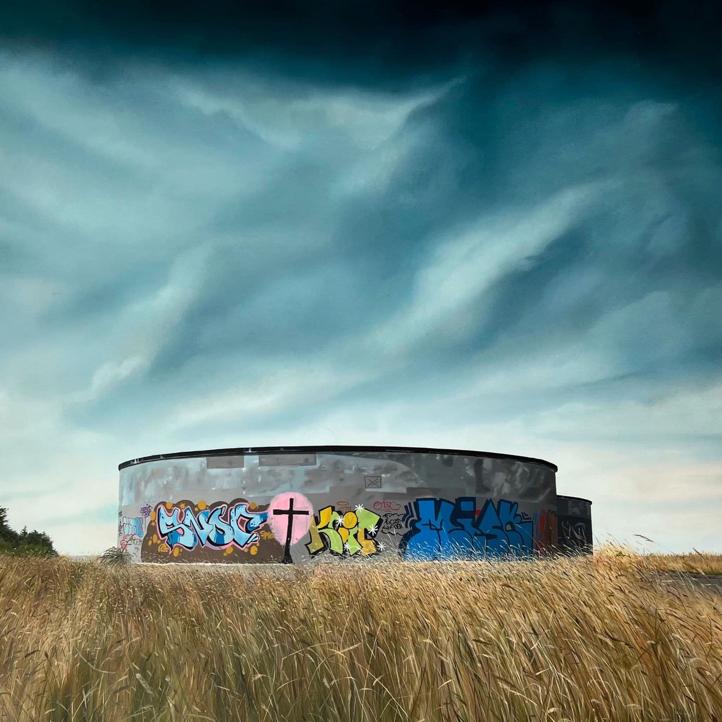 Close up of a round concrete structure with graffiti on a grassy field under a dramatic sky.