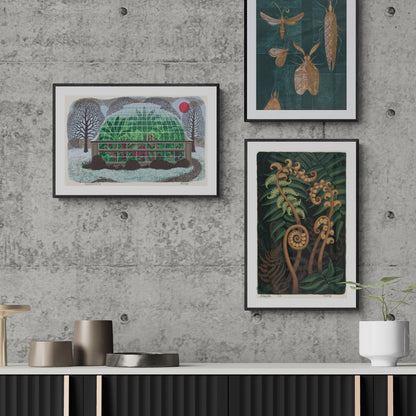 Three framed Eileen Mayo artworks on a concrete wall with a table and plant in the foreground.