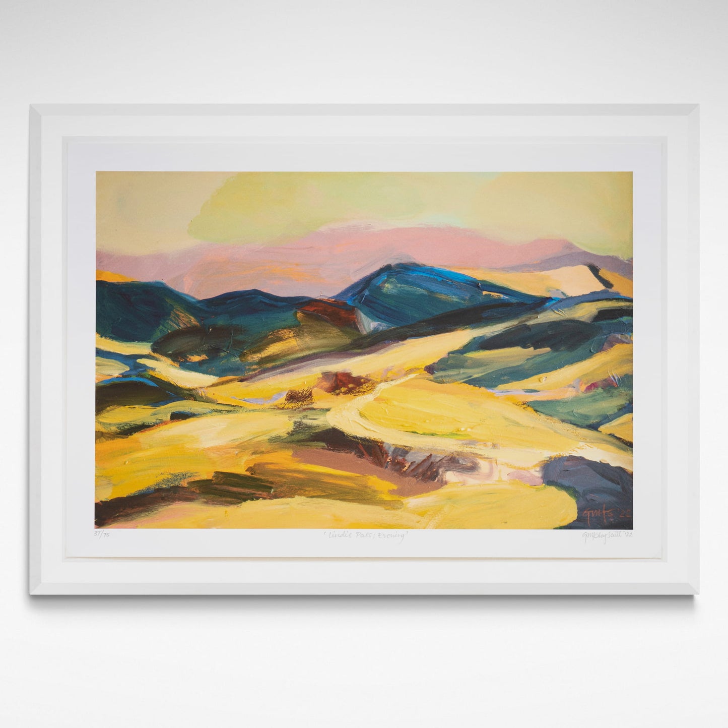 Framed colourful evening landscape print in yellow and gold with blue hills and pink sky.