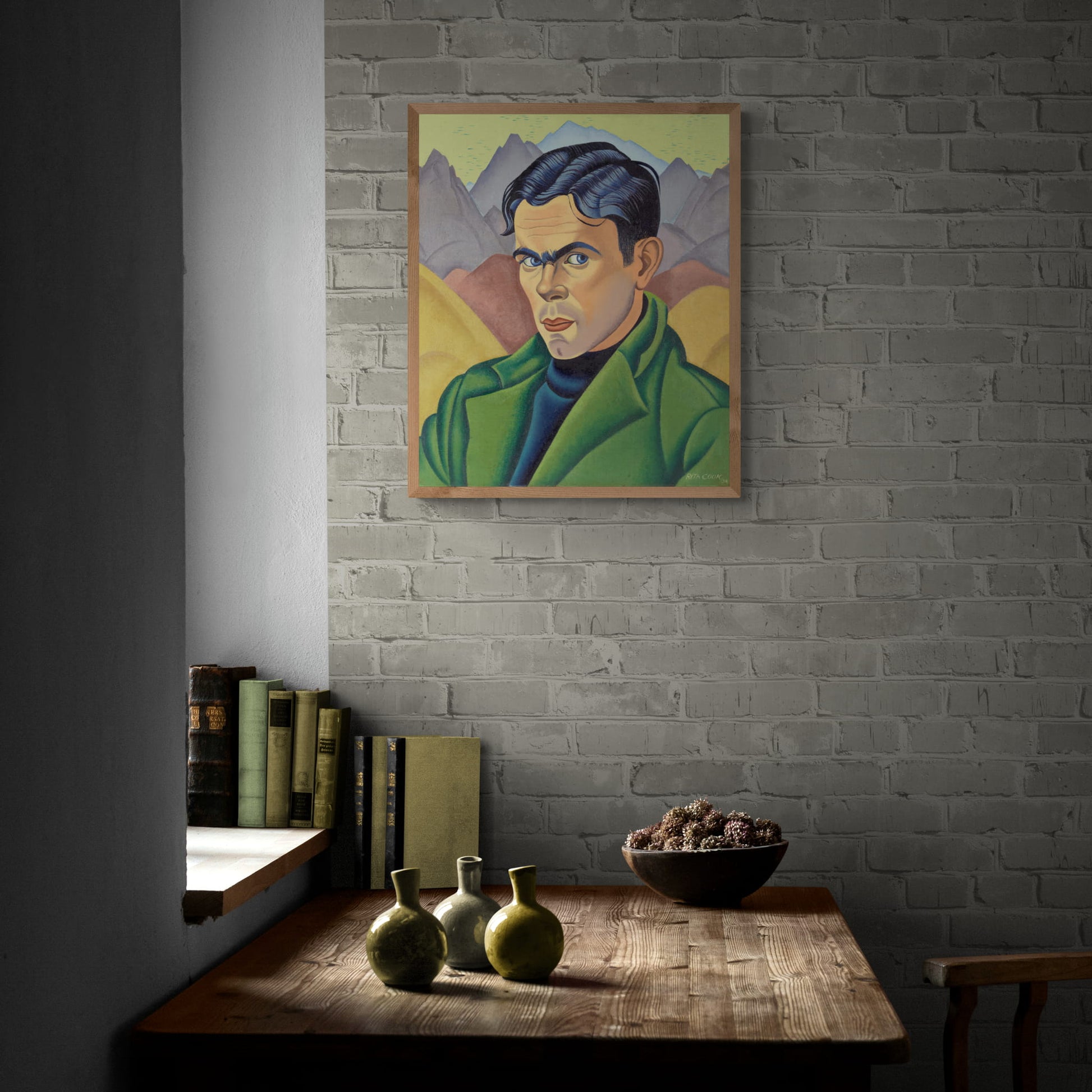 Framed portrait of a man in a green coat against a background of mountains hanging on brick wall.